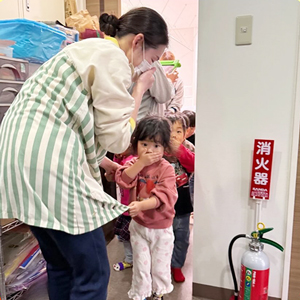 口に手を当てて避難訓練をする子どもたちと保育士