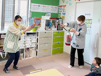 消火器を見せ、物語の中の火を消す保育士たち