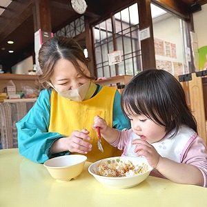 先生に見守られながらスプーンでじょうずに給食を食べる子ども