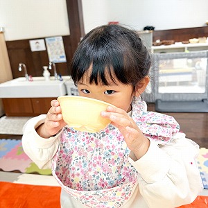 お椀を両手に持って汁物を飲む子ども