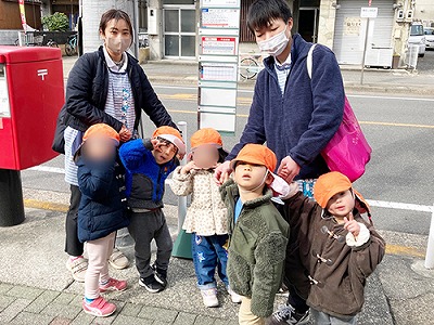 保育士と一緒にバス停でバスを待つ子どもたち