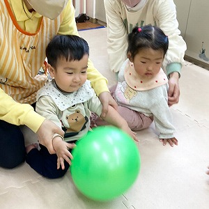 保育士と一緒にボールに触れる子どもたち