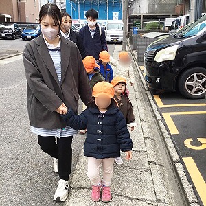 保育士を手をつないで道を歩く子どもたち