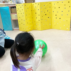 屏風に向かってボールを転がす子ども