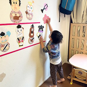 壁に貼ったおひなさまを飾り付ける子ども