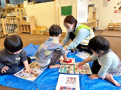 シートを広げておひなさまの制作をする子どもたちの保育士