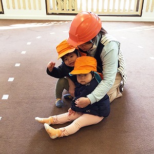 ヘルメットを被り園児と身を寄せ合う保育士
