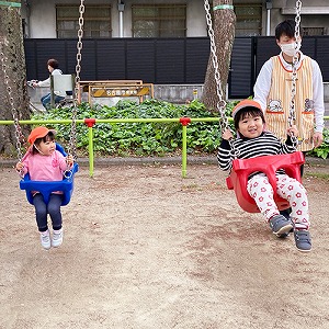 お友だちを並んでブランコをこぐ子どもたち