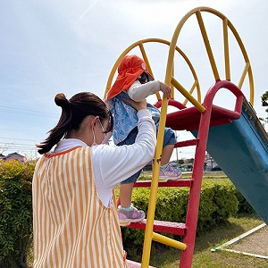 保育士に支えられて公園の滑り台の階段にのぼる子ども