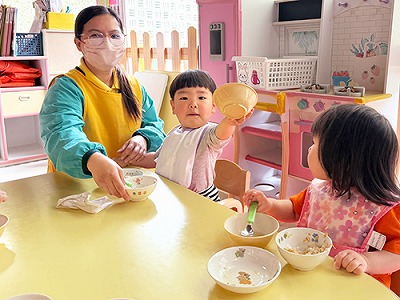 器を突き出しておかわりをせがむ子どもとそれをみつめるお友だち