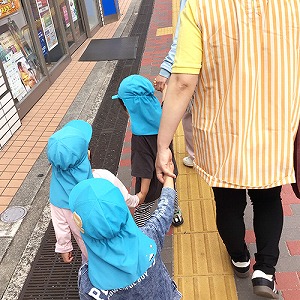 保育士と手を繋いで散歩にでかける園児たち