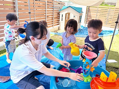 プールを囲んで水遊びを楽しむ保育士と子どもたち
