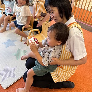 先生の膝の上で誕生日ケーキのおもちゃを持つ子ども