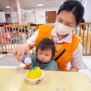 膝に乗せた子どもと一緒にかき氷を作る保育士