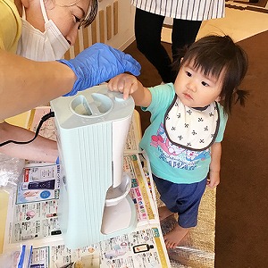 先生と一緒にかき氷器のボタンを押す子ども