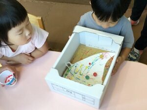 箱の中のビー玉を転がす子どもと見守るお友だち