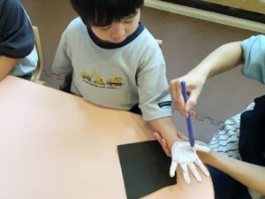 手のひらに絵の具をつけてもらう子ども