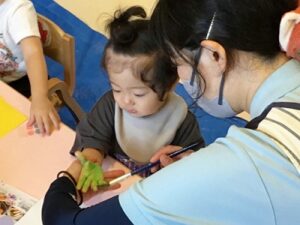 先生に手のひらに絵の具をつけてもらう子ども